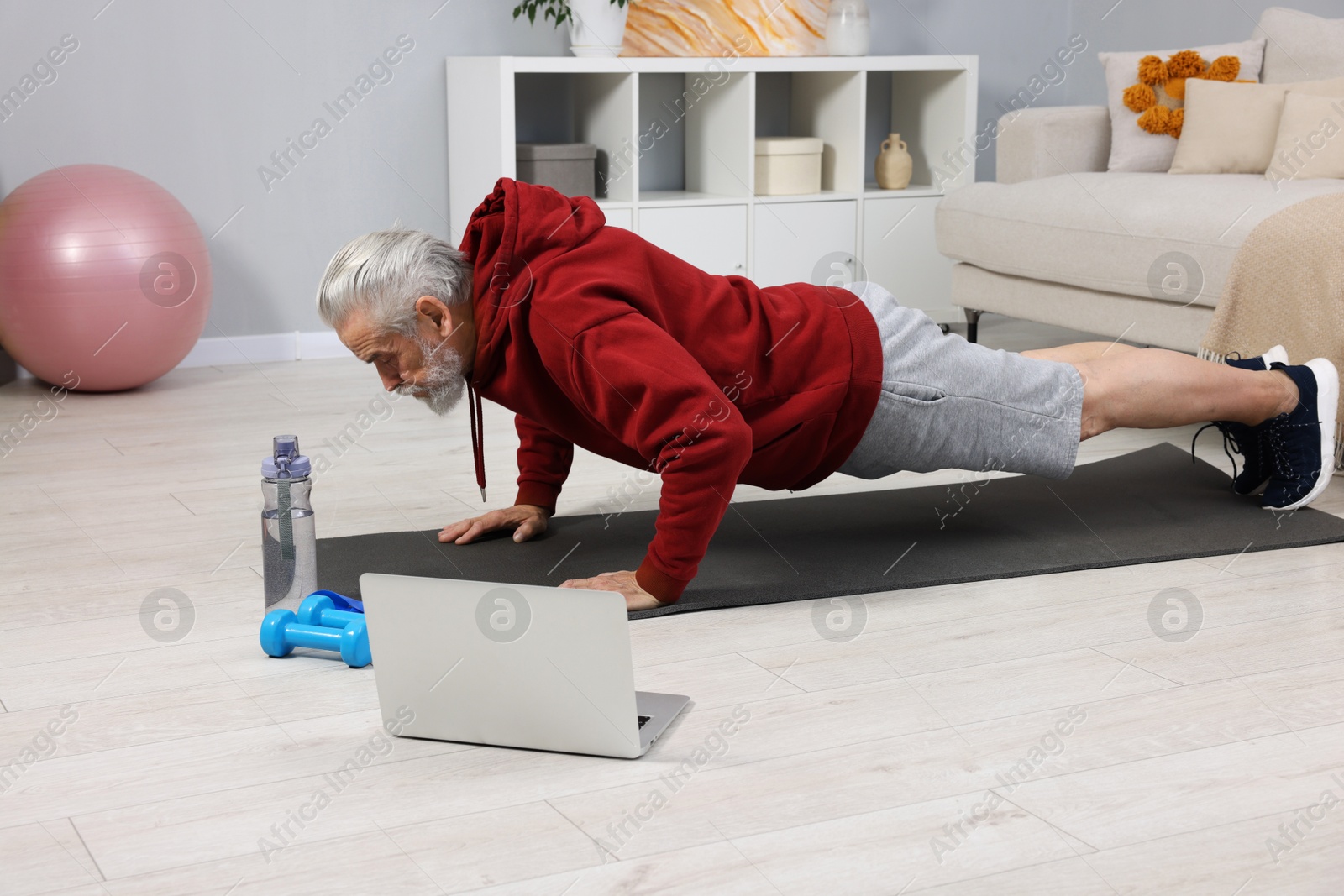 Photo of Elderly man exercising near laptop at home