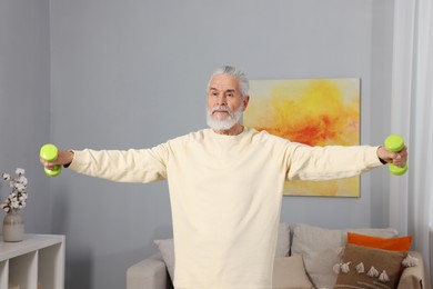 Elderly man exercising with dumbbells at home