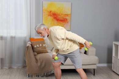 Photo of Elderly man exercising with dumbbells at home