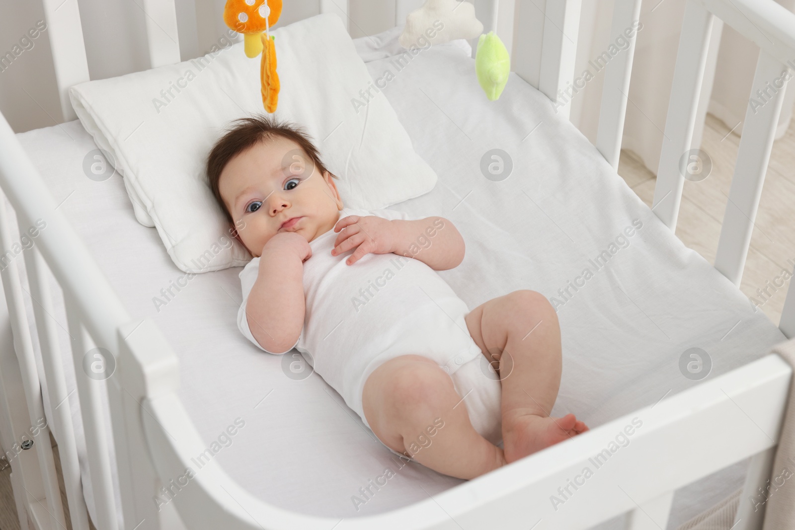 Photo of Cute little baby in crib with cot mobile at home