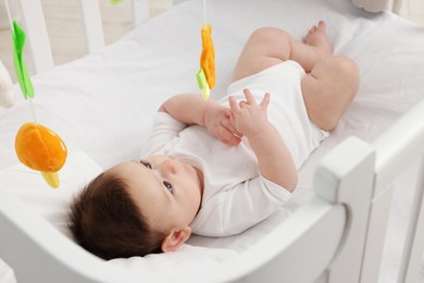 Photo of Cute little baby in crib with cot mobile at home