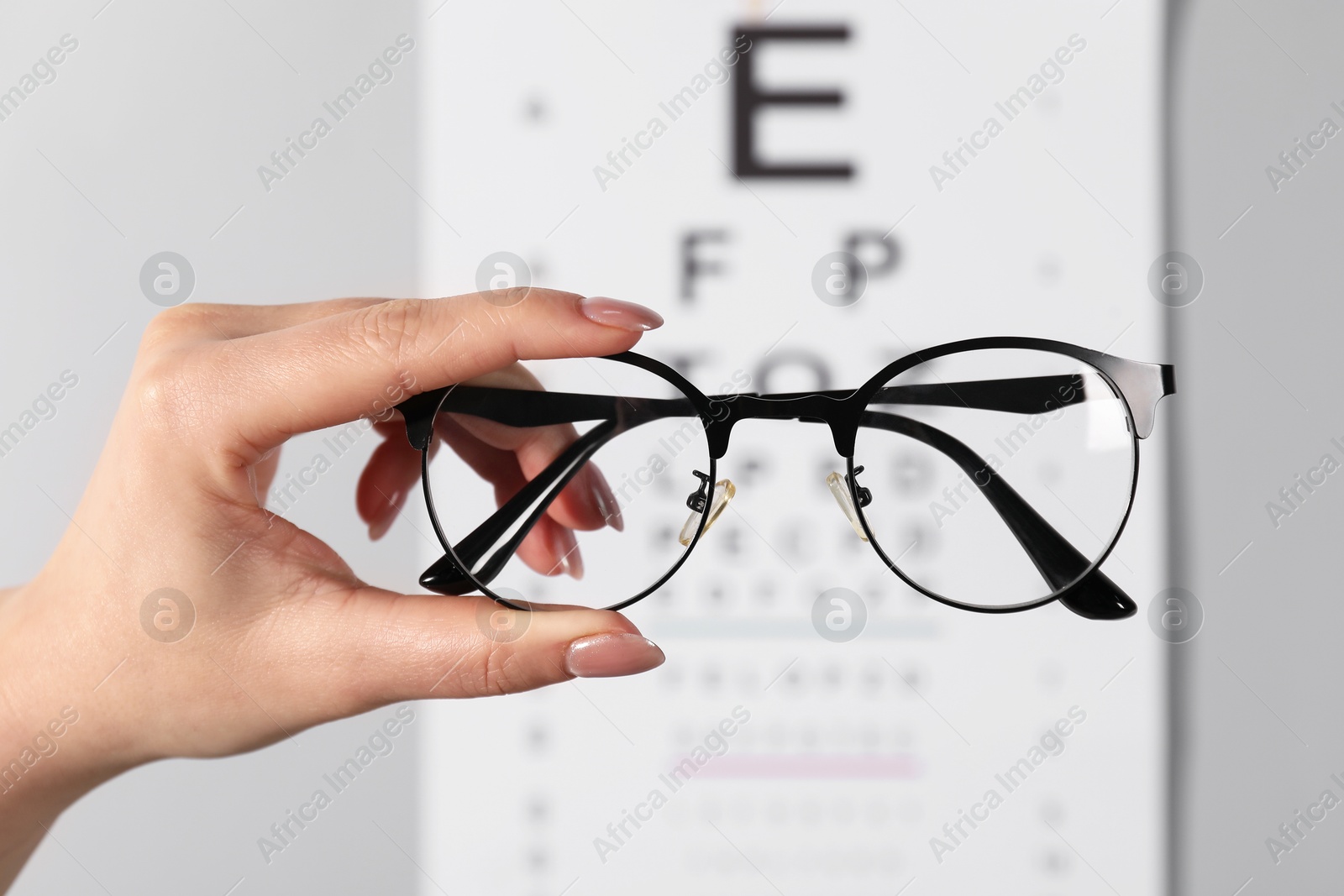 Photo of Woman holding glasses against vision test chart on grey background, closeup