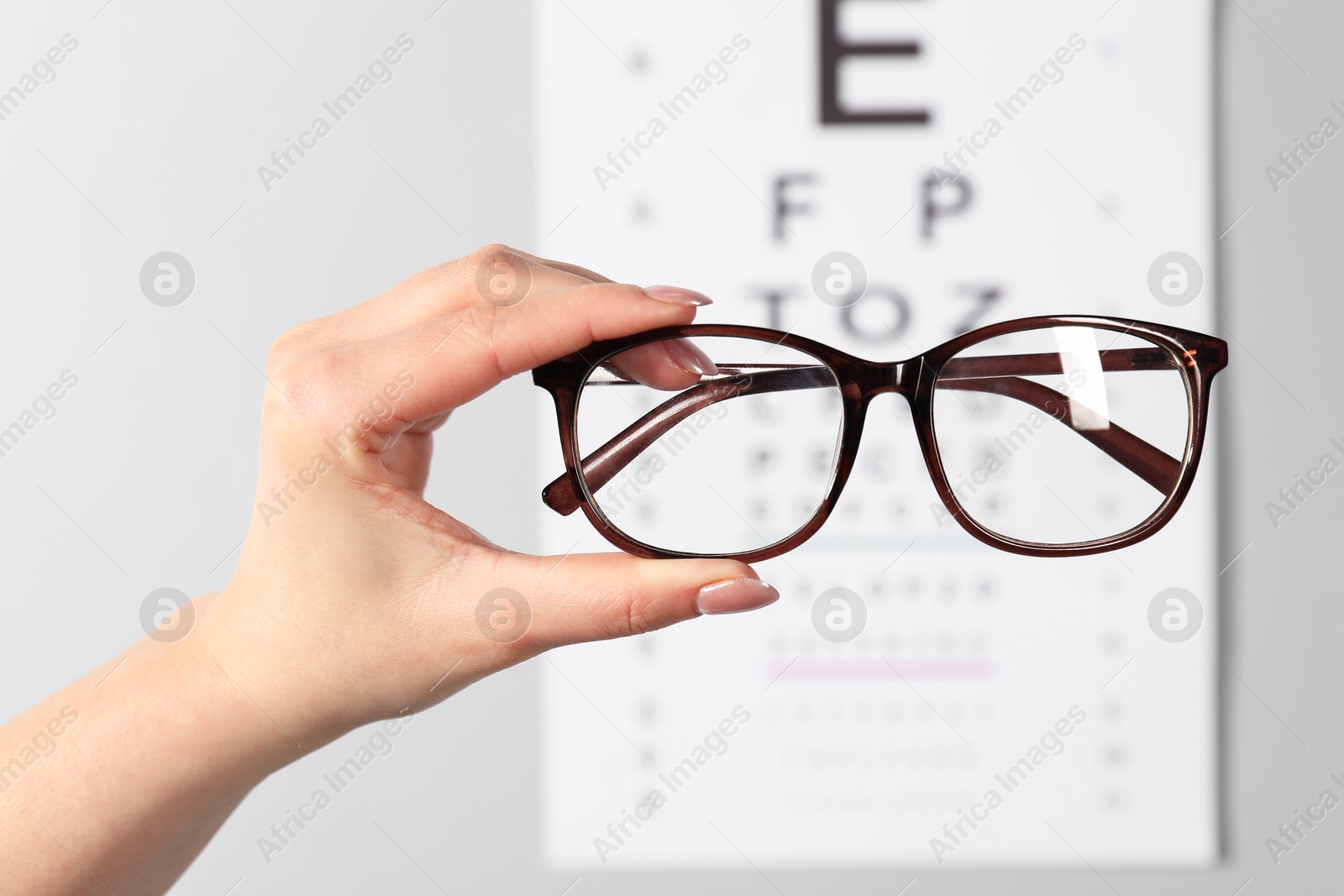 Photo of Woman holding glasses against vision test chart on grey background, closeup