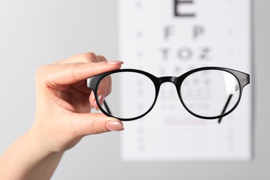 Photo of Woman holding glasses against vision test chart on grey background, closeup