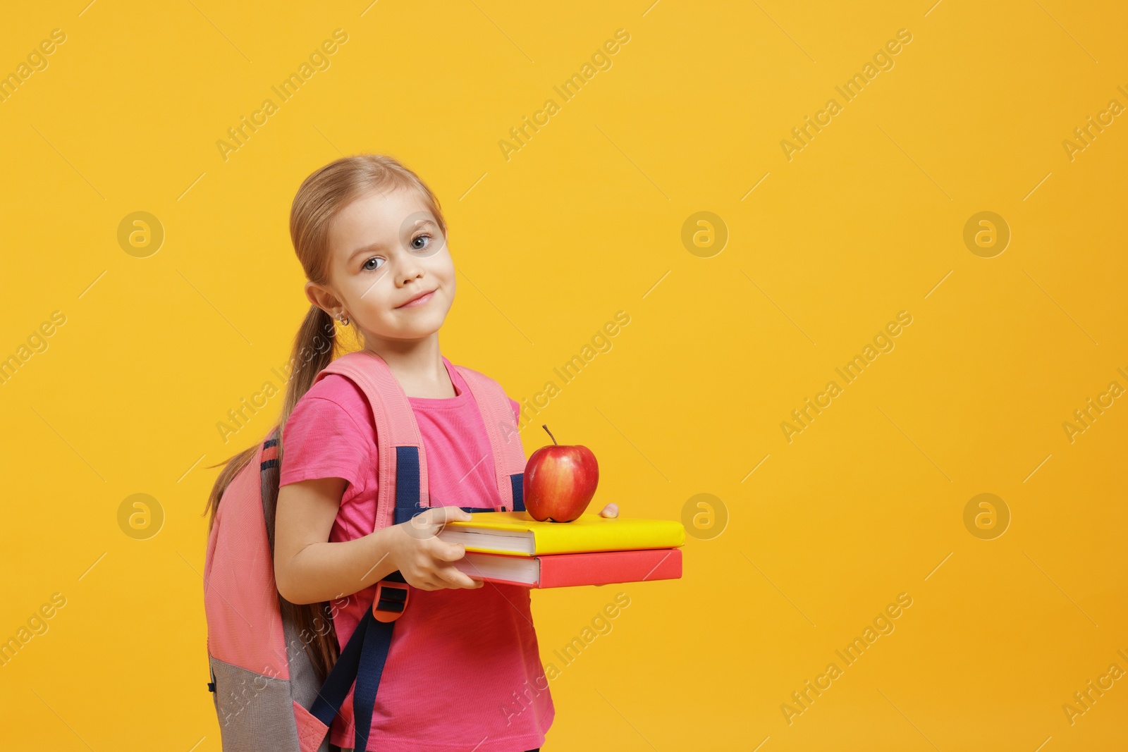 Photo of Cute little girl with books and apple on orange background. Space for text