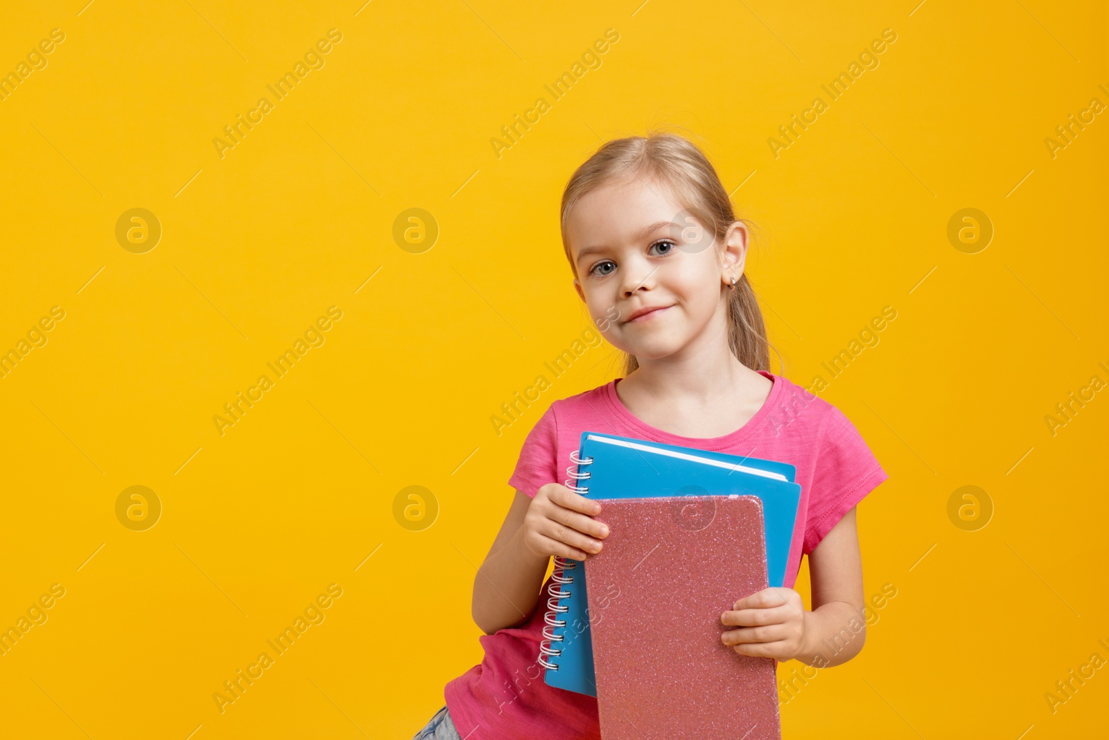 Photo of Cute little schoolgirl with books on orange background. Space for text