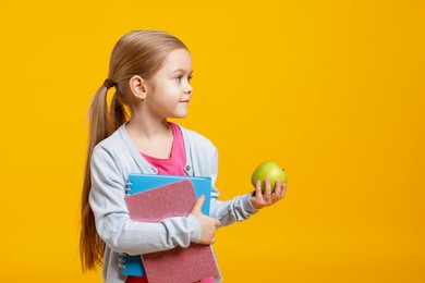 Photo of Cute little girl with books and apple on orange background. Space for text