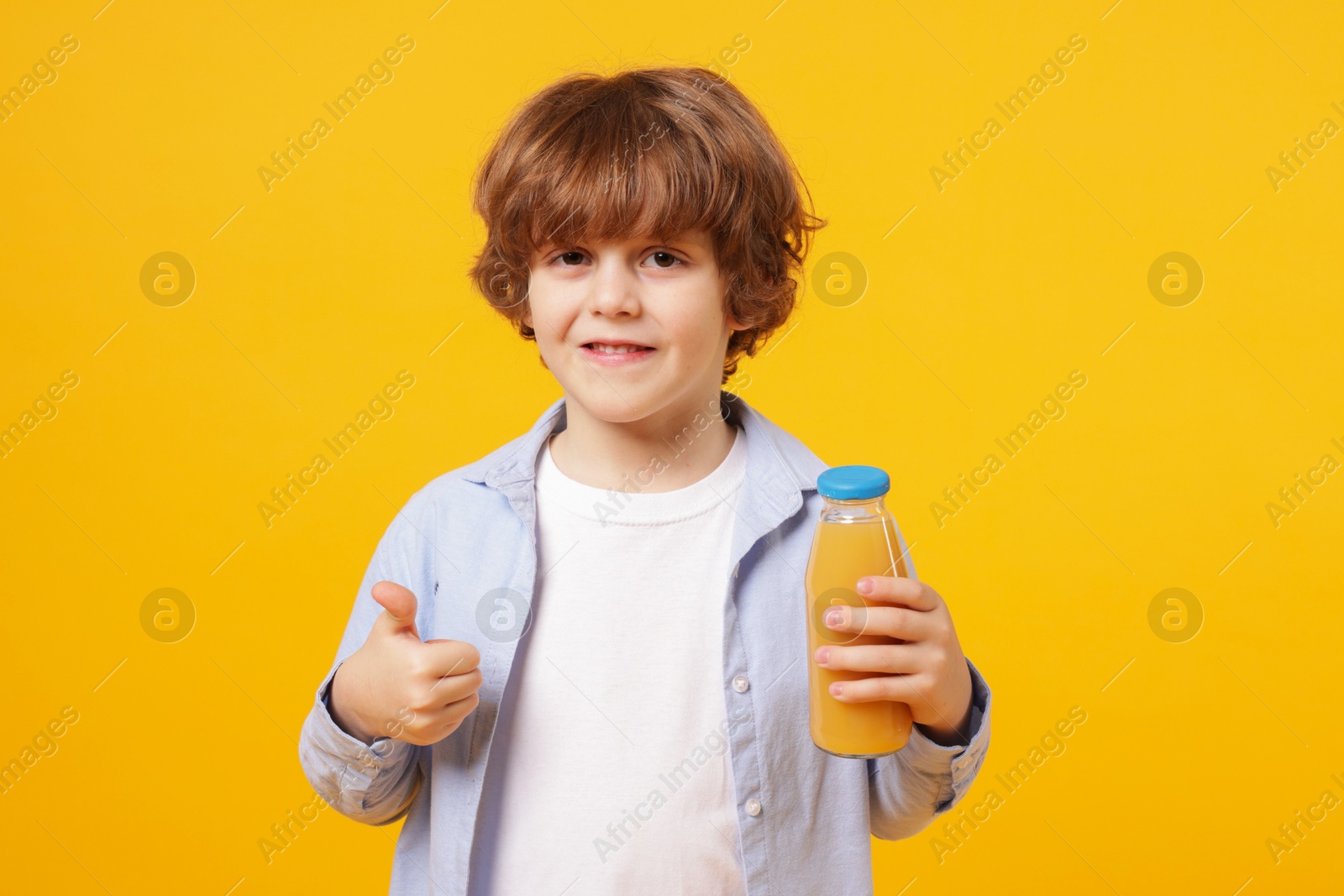 Photo of Little boy with drink showing thumbs up on orange background