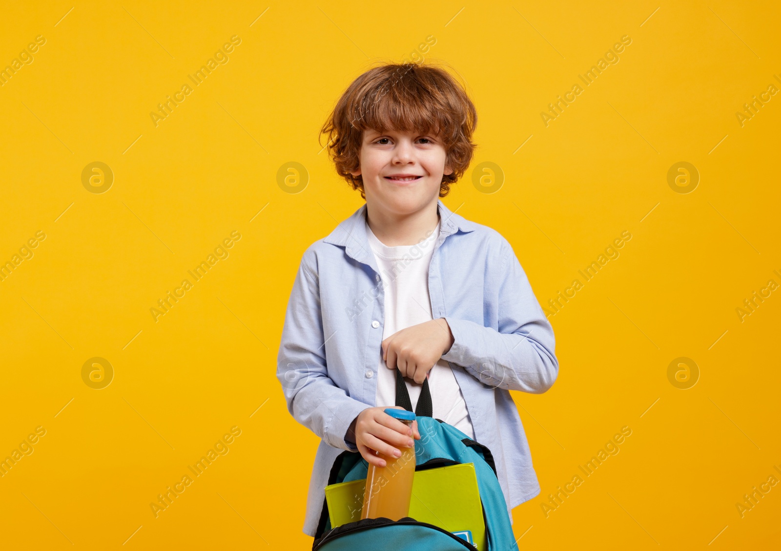 Photo of Little boy packing drink into backpack on orange background