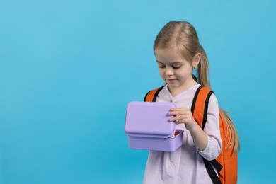 Photo of Cute little girl with lunch box on light blue background. Space for text