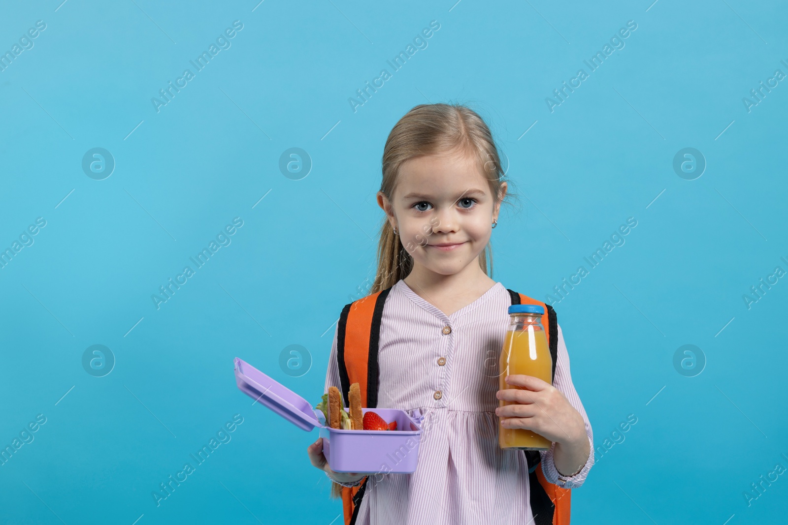 Photo of Cute little girl with lunch box and drink on light blue background