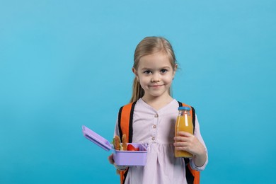 Photo of Cute little girl with lunch box and drink on light blue background