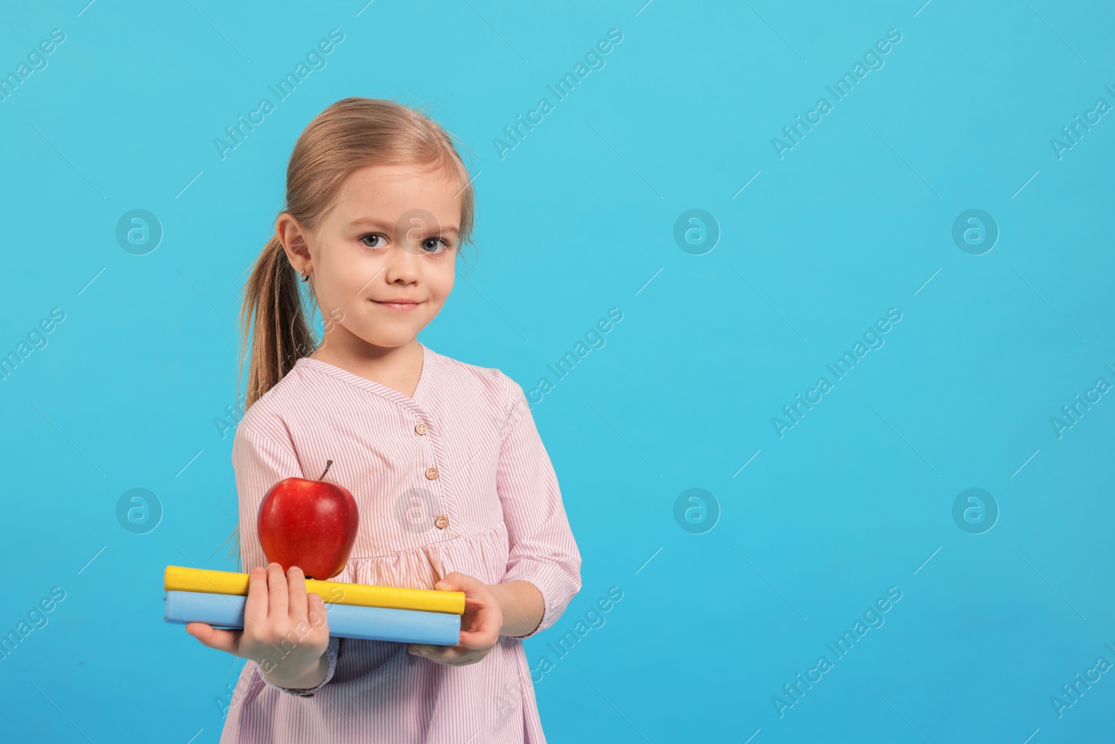 Photo of Cute little girl with books and apple on light blue background. Space for text