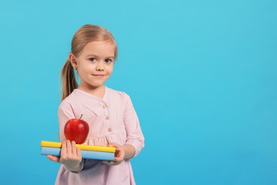 Photo of Cute little girl with books and apple on light blue background. Space for text