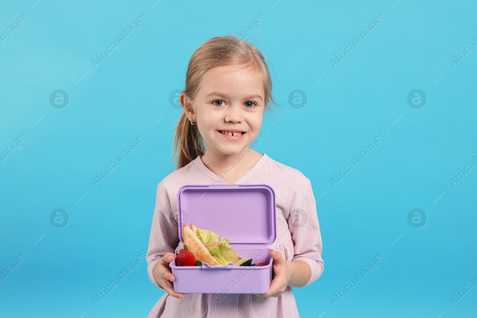 Photo of Cute little girl with lunch box on light blue background