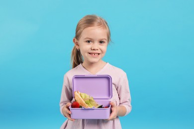 Cute little girl with lunch box on light blue background