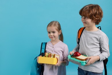 Cute little children with lunch boxes on light blue background