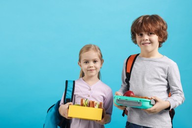 Photo of Cute little children with lunch boxes on light blue background. Space for text