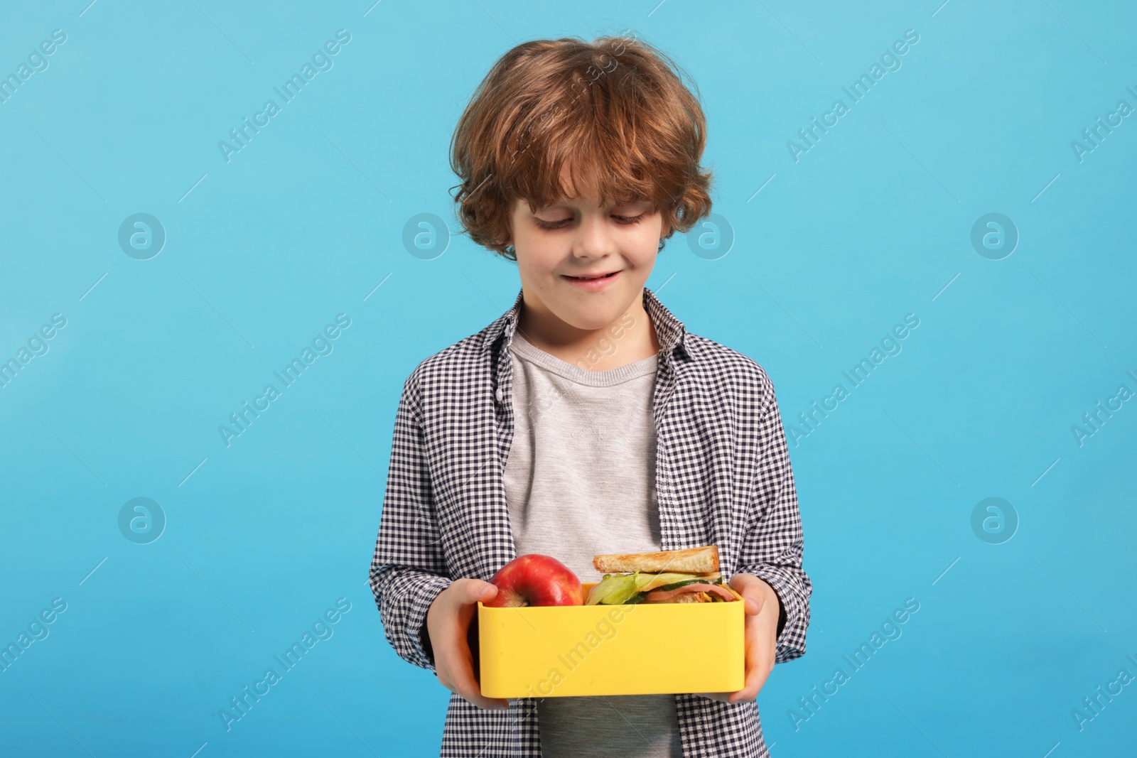 Photo of Cute little boy with lunch box on light blue background