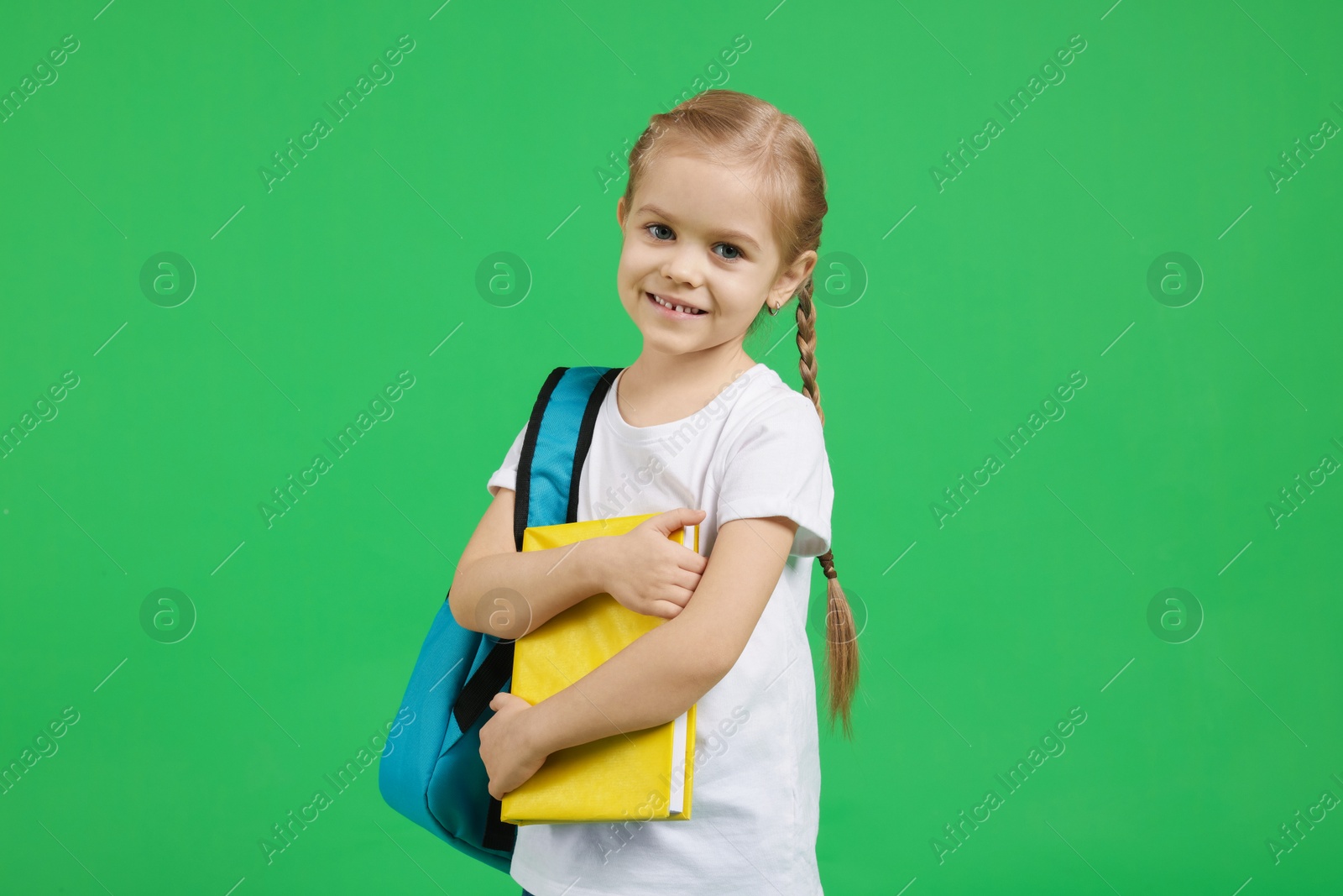 Photo of Cute little girl with backpack and book on green background