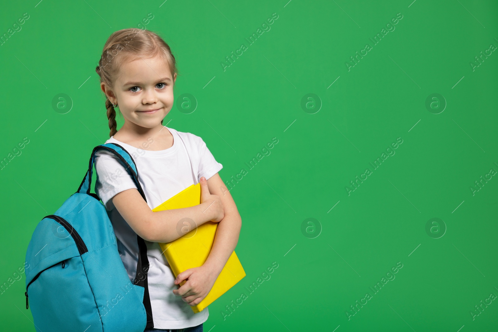 Photo of Cute little girl with backpack and book on green background. Space for text