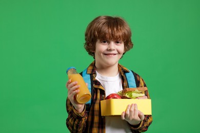 Cute little boy with lunch box and drink on green background