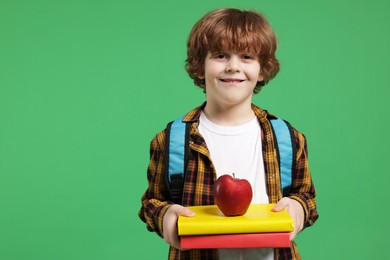 Photo of Cute little boy with books and apple on green background. Space for text