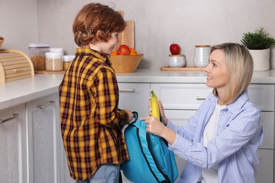 Mother giving her son banana for school snack in kitchen