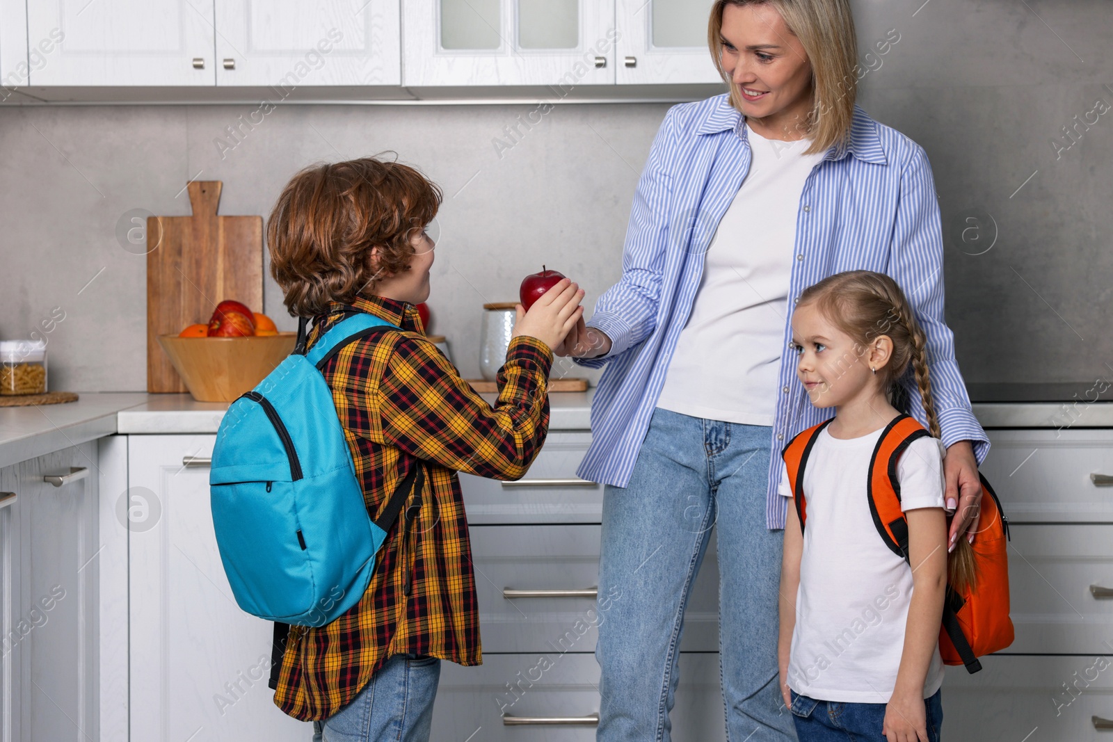 Photo of Mother giving her children fruits for school snacks in kitchen