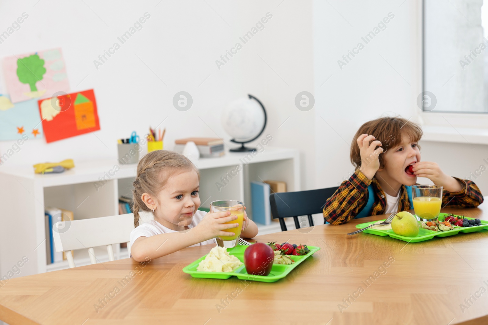 Photo of Cute little children eating lunch at wooden table in school