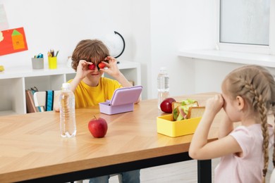 Cute little children eating lunch at wooden table in school