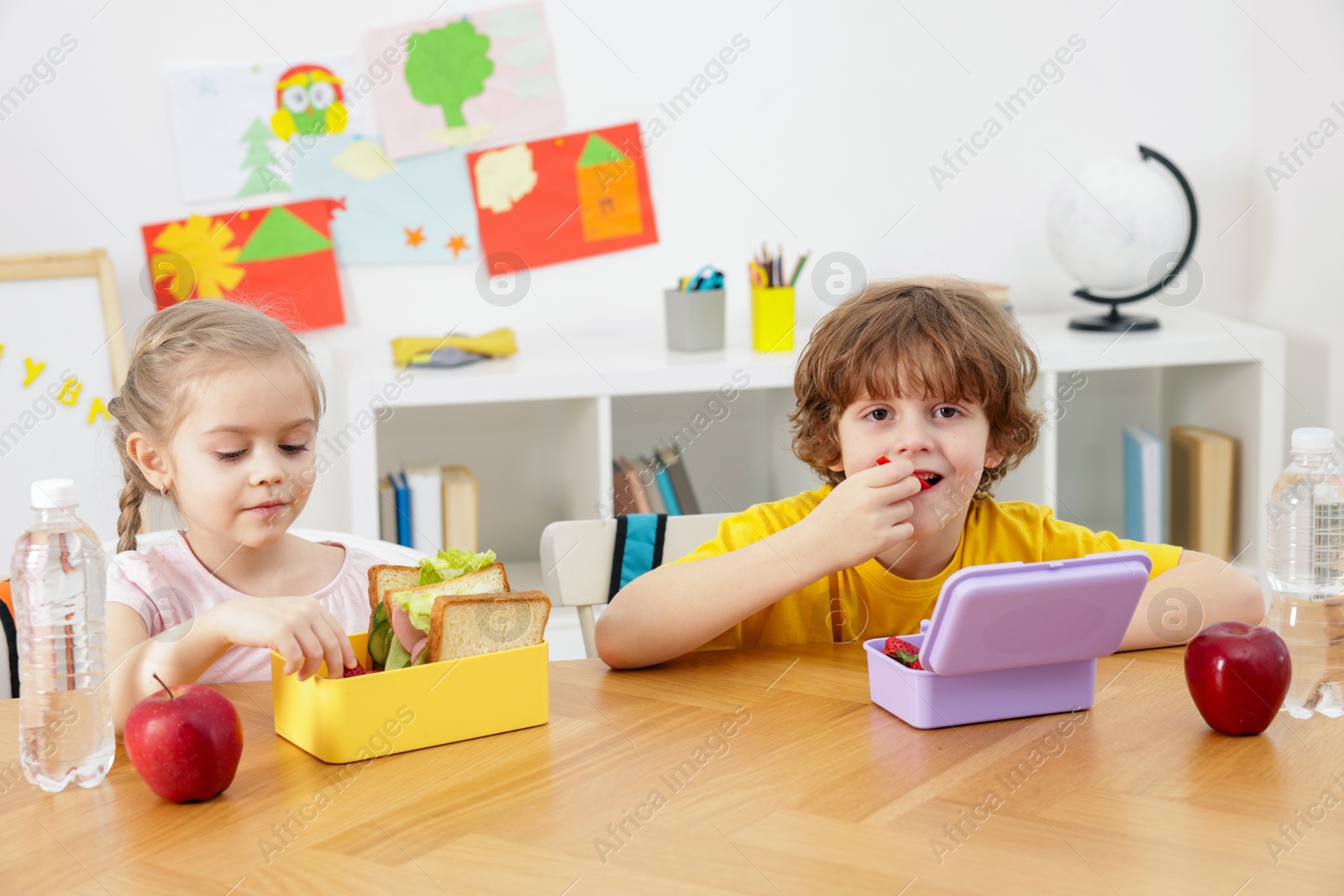 Photo of Cute little children eating lunch at wooden table in school