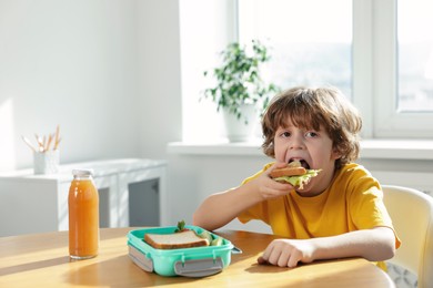 Cute little boy eating lunch at wooden table in school. Space for text