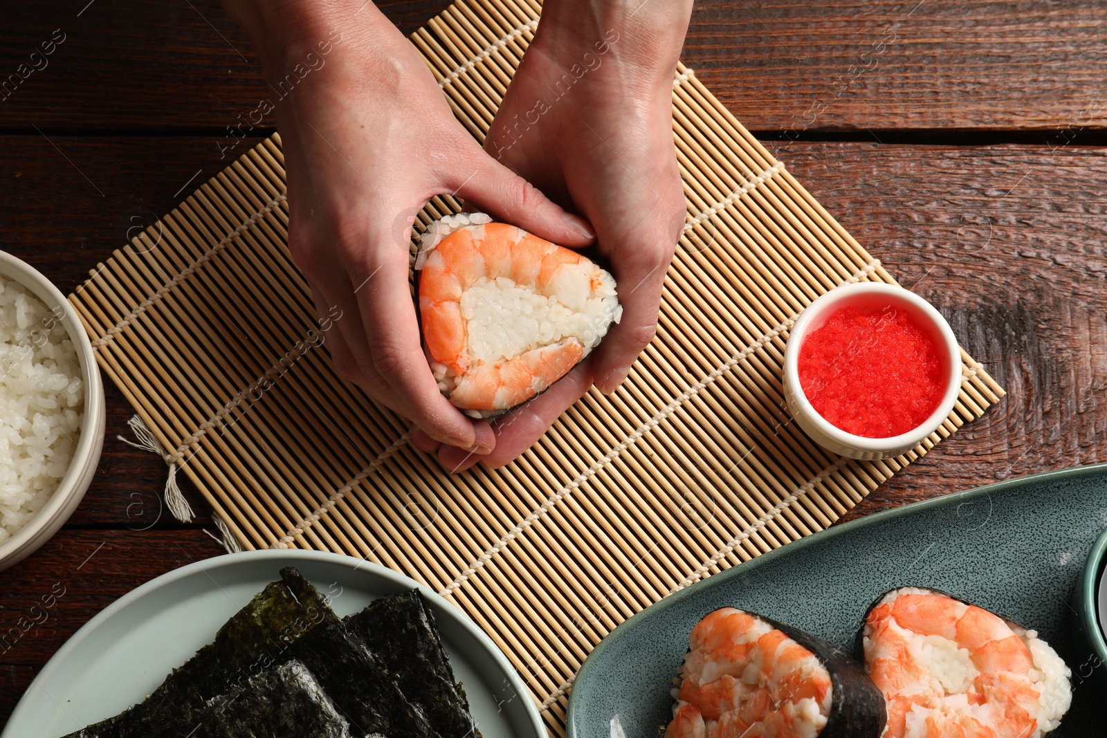Woman holding tasty onigiri (Japanese rice ball) with shrimp at wooden table, top view Photo of Woman holding tasty onigiri (Japanese rice ball) with shrimp at wooden table, top view