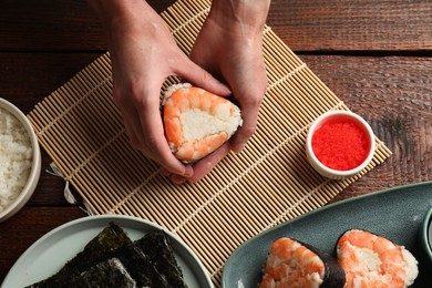 Photo of Woman holding tasty onigiri (Japanese rice ball) with shrimp at wooden table, top view
