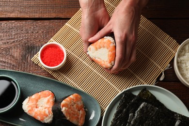 Photo of Woman holding tasty onigiri (Japanese rice ball) with shrimp at wooden table, top view