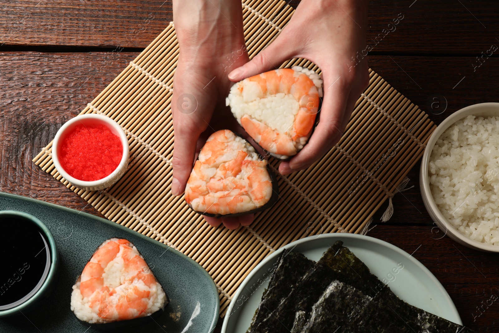 Woman holding tasty onigiri (Japanese rice balls) with shrimps at wooden table, top view Photo of Woman holding tasty onigiri (Japanese rice balls) with shrimps at wooden table, top view