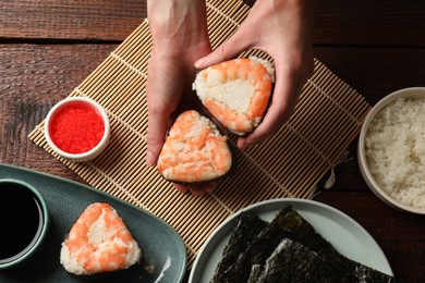 Photo of Woman holding tasty onigiri (Japanese rice balls) with shrimps at wooden table, top view