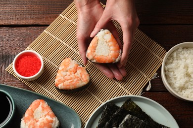 Photo of Woman holding tasty onigiri (Japanese rice ball) with shrimp at wooden table, top view