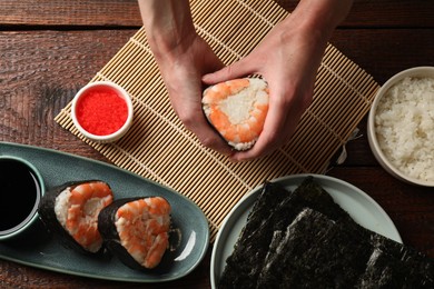 Photo of Woman holding tasty onigiri (Japanese rice ball) with shrimp at wooden table, top view