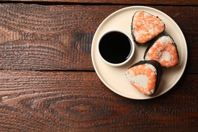 Photo of Tasty onigiri (Japanese rice balls) with shrimps and soy sauce on wooden table, top view. Space for text