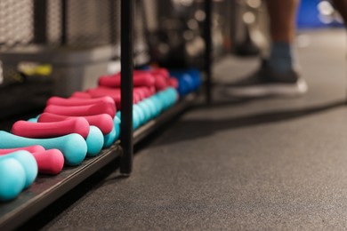 Colorful dumbbells on shelf and man in gym