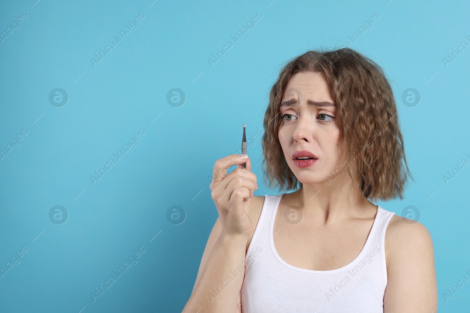 Photo of Excited woman looking at tweezers on light blue background, space for text. Mustache removal tool