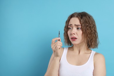 Excited woman looking at tweezers on light blue background, space for text. Mustache removal tool