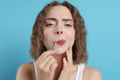 Photo of Beautiful woman plucking her mustache with tweezers on light blue background