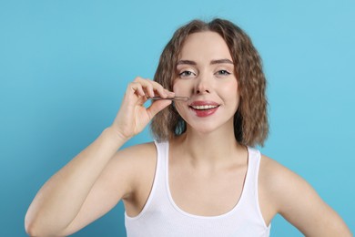 Smiling woman plucking her mustache with tweezers on light blue background