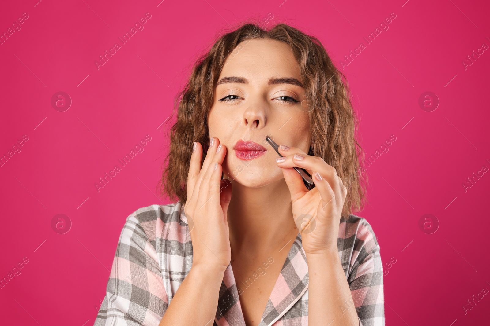 Photo of Beautiful woman plucking her mustache with tweezers on pink background