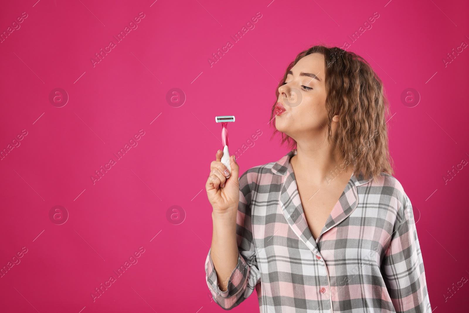 Photo of Funny woman blowing onto razor on pink background, space for text. Hair removal tool