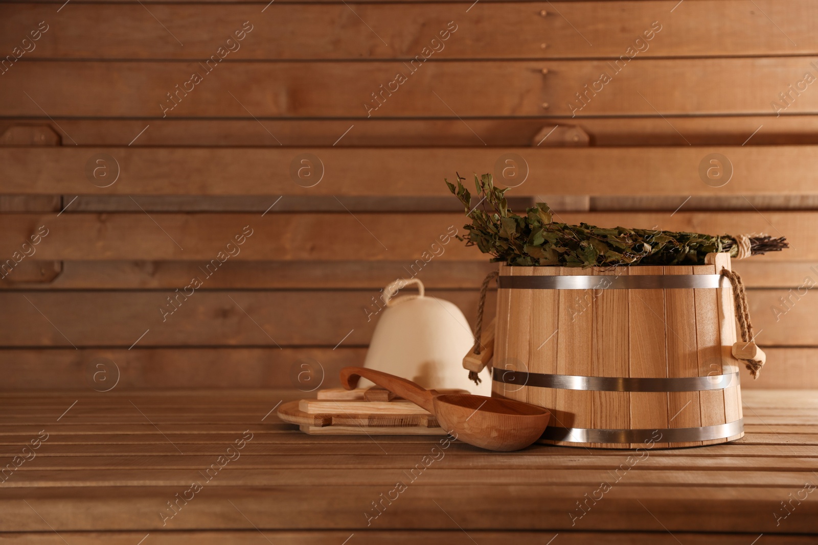 Photo of Bucket, ladle and whisk on wooden bench in sauna. Space for text