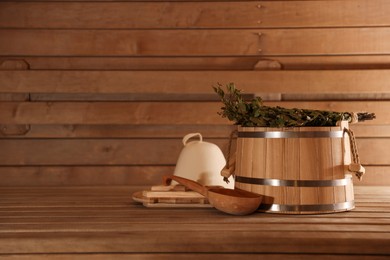 Bucket, ladle and whisk on wooden bench in sauna. Space for text